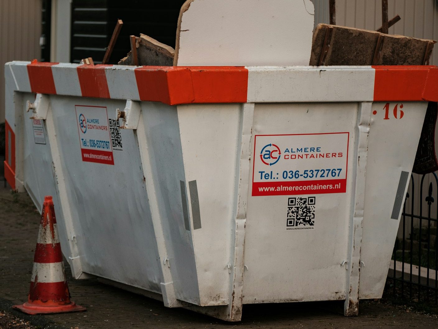 Yellow-white open-top skip with traffic cone on a residential pavement