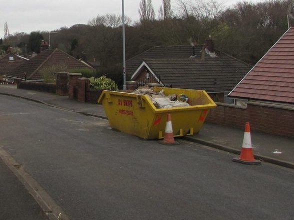 Yellow builders' skip on a UK residential street with traffic cones